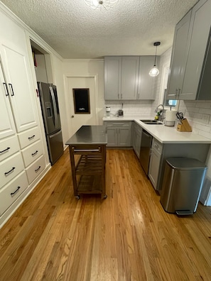 Una cocina con armarios blancos, un refrigerador de acero inoxidable, una mesa de madera y un lavavajillas.