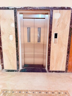 Un ascensor con panel de control, acabados metálicos y suelo de aspecto marmol.