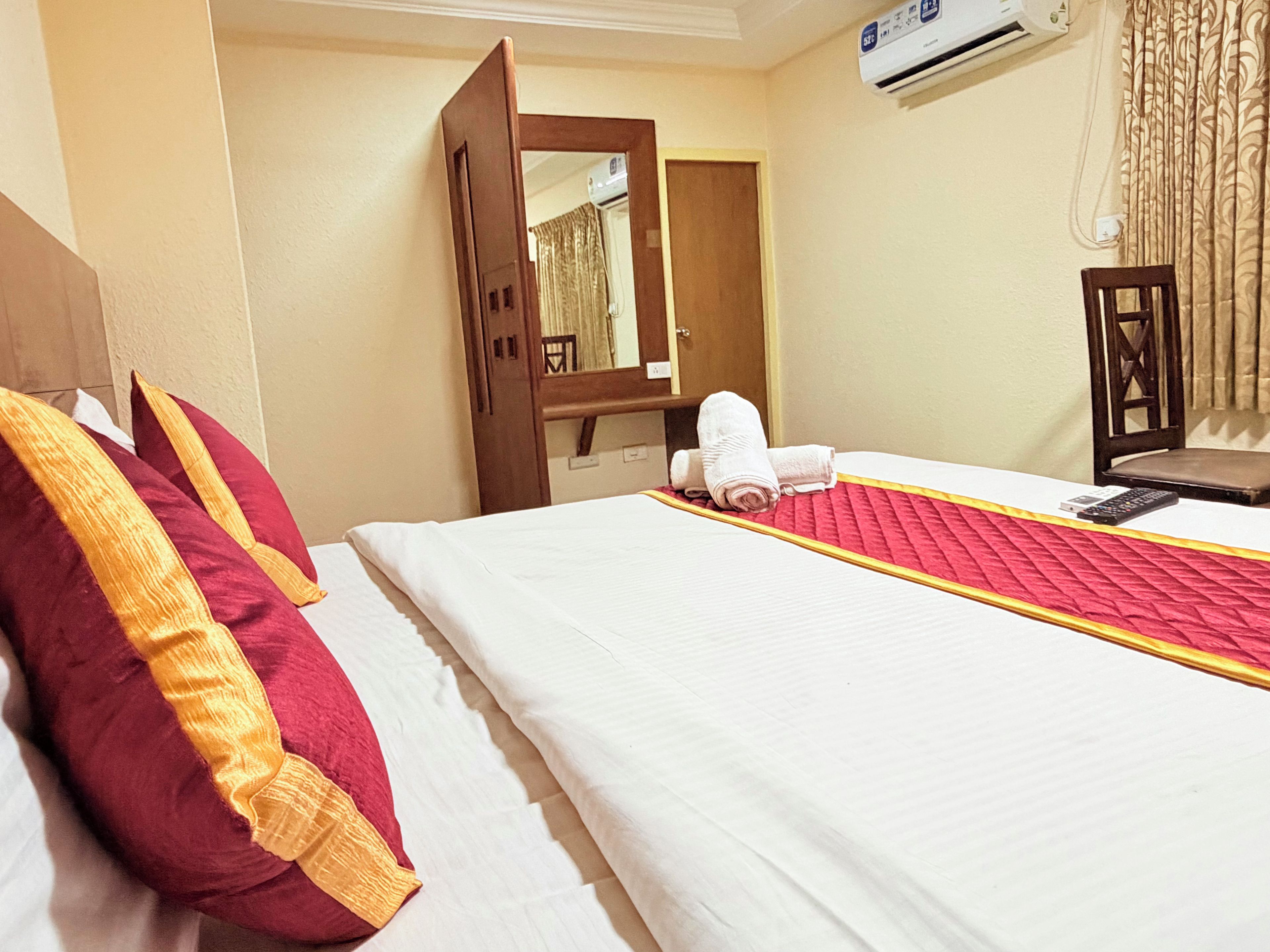 Una habitación de hotel con cama, almohadas, mesita de noche, espejo y aire acondicionado.