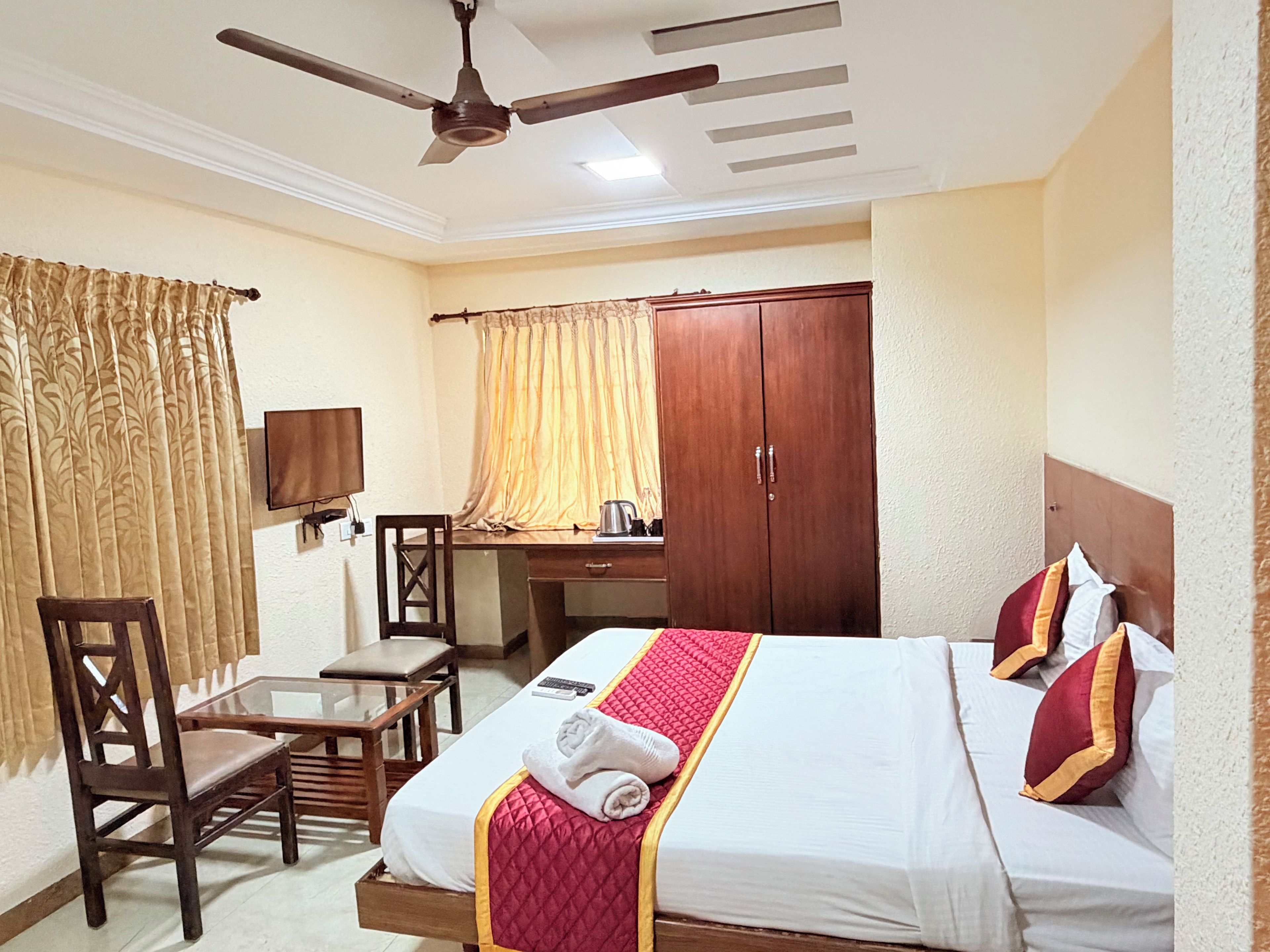 A hotel room with a bed, a desk, a chair, a wardrobe, and a ceiling fan.