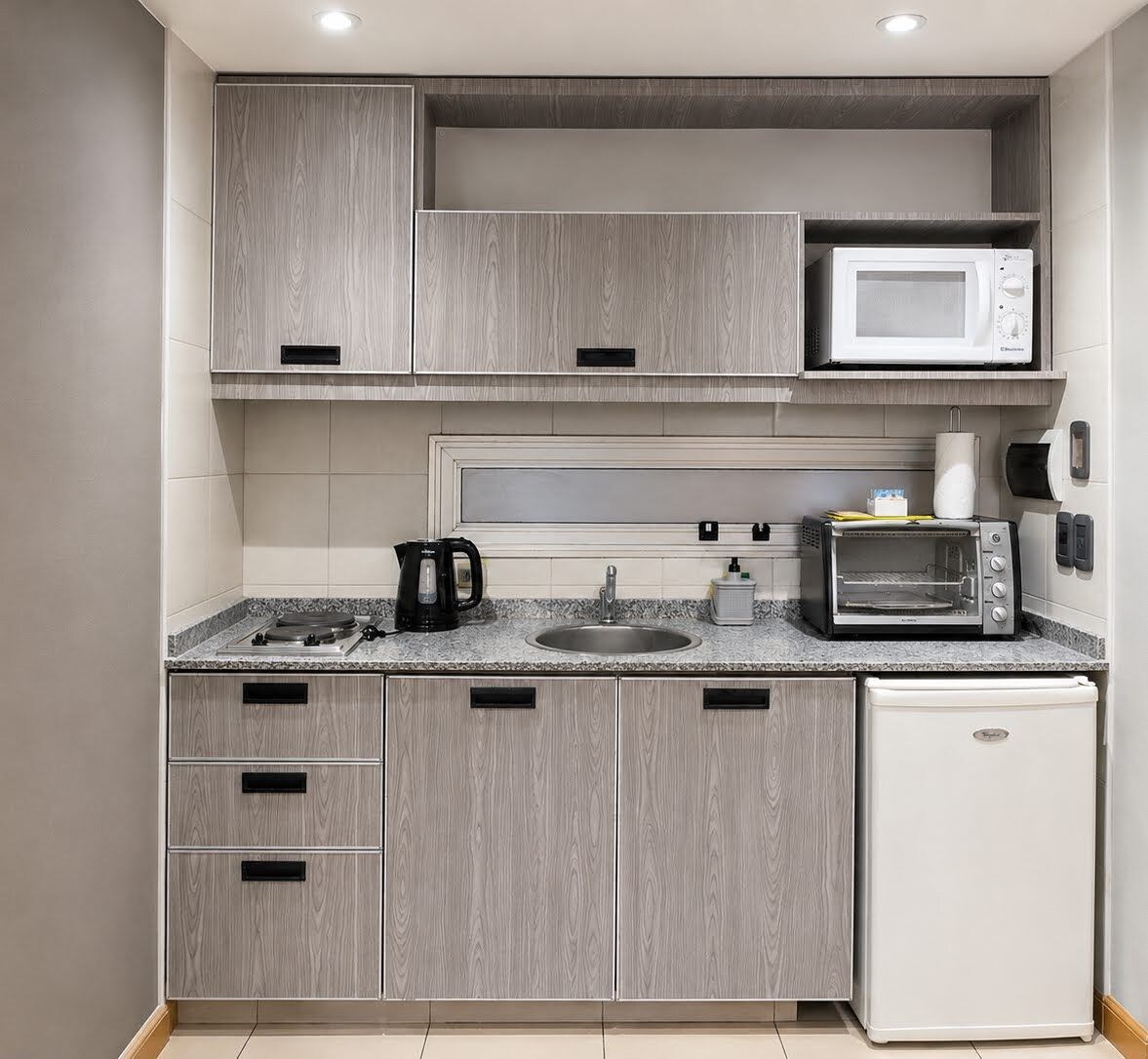 Eine kleine Küche mit Mikrowelle, Toaster, Wasserkocher und kleinem Kühlschrank.