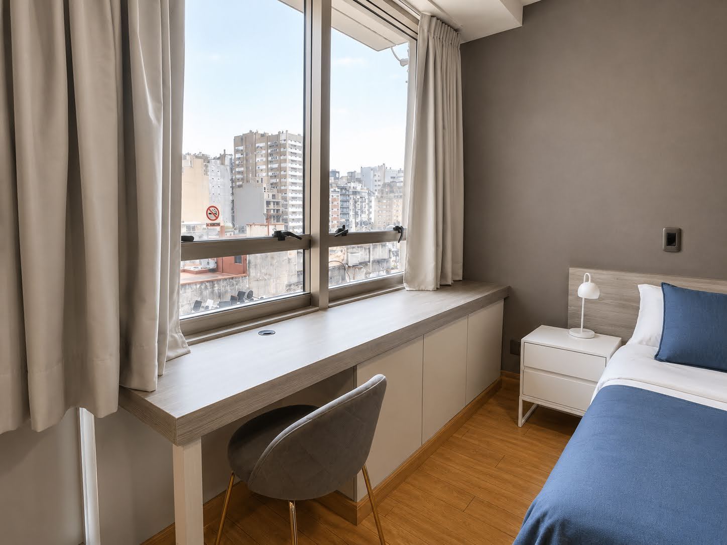 Ein Schlafzimmer mit Bett, Schreibtisch, Stuhl, Nachttisch und einem Fenster mit Vorhängen.