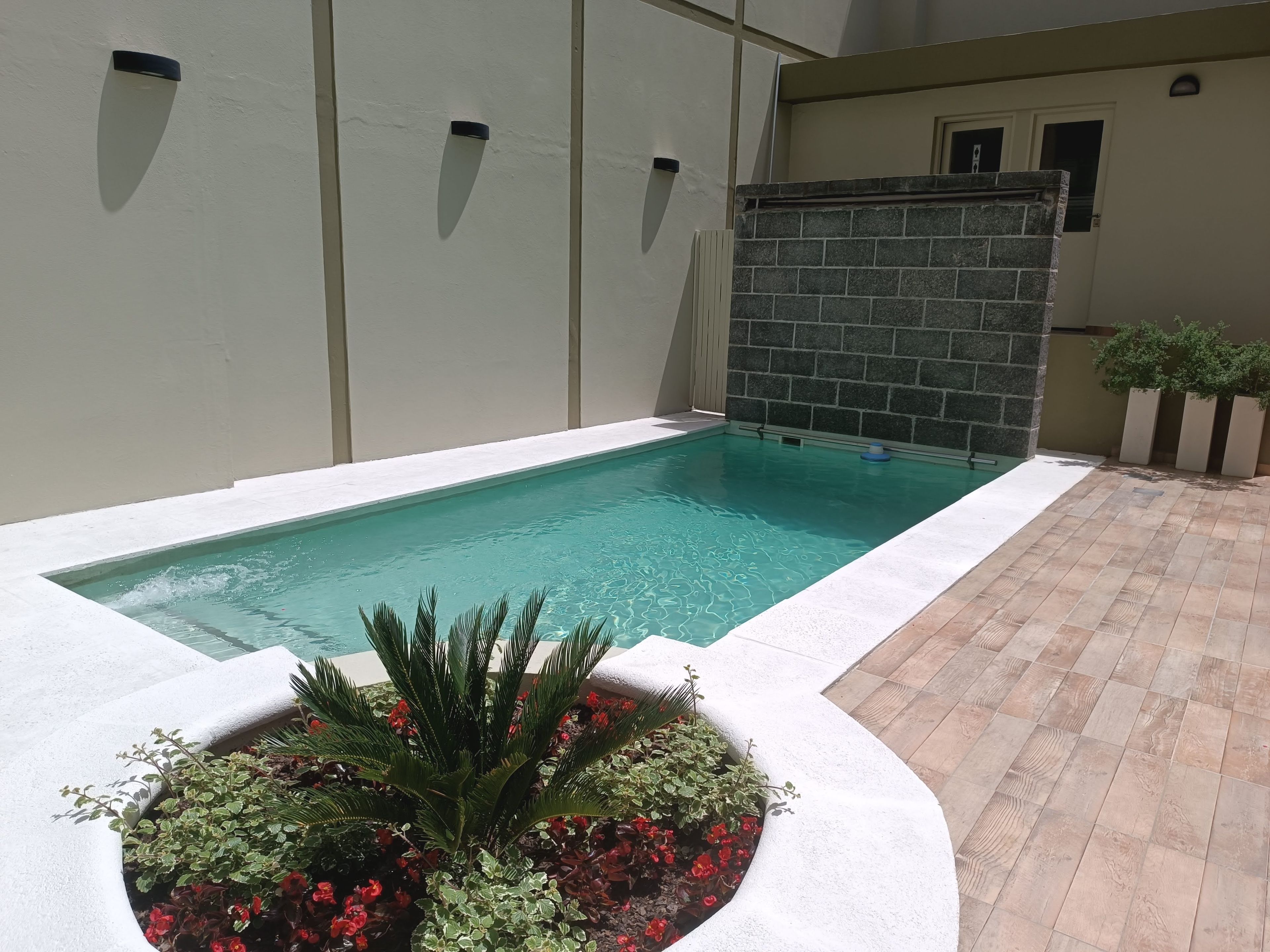 Ein rechteckiger Swimmingpool mit weißer Umrandung, umgeben von einer gefliesten Terrasse.
