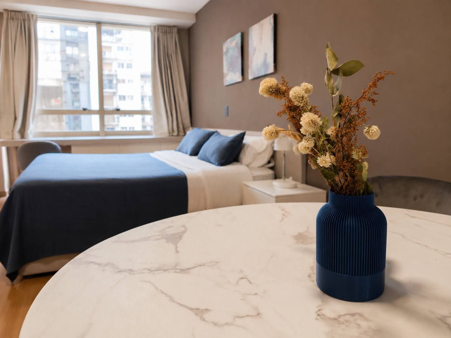 A hotel room with a bed, a nightstand, a vase with flowers, and a window with curtains.