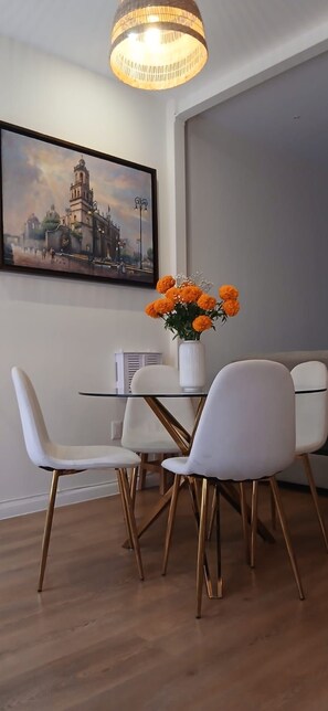 Ein Essbereich mit Tisch, Stühlen, einer Blumenvase und einem Bild an der Wand.