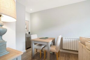 A dining area with a table, chairs, a lamp, a radiator, and a framed picture on the wall. - Cosy Keswick 1BR|Sleeps 2| by Stay with Us (Keswick)
