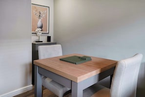 A dining table with a stack of green notebooks, a vase with flowers, and a bust sculpture on a shelf. - Cosy Keswick 1BR|Sleeps 2| by Stay with Us (Keswick)