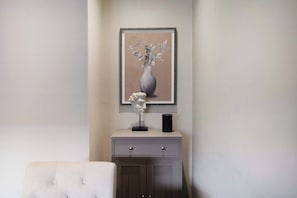A framed artwork of a vase with flowers on a wall, a bust sculpture on a cabinet, and a white upholstered chair. - Cosy Keswick 1BR|Sleeps 2| by Stay with Us (Keswick)