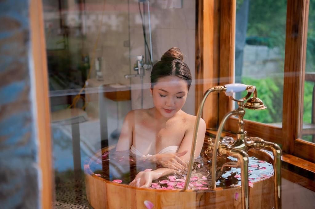 Eine Person in einer Badewanne mit Rosenblättern, einer Duschbrause und einer Holzvertäfelung.