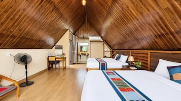 Una habitación con techo inclinado, una cama con colcha colorida, un escritorio con silla y un ventilador.
