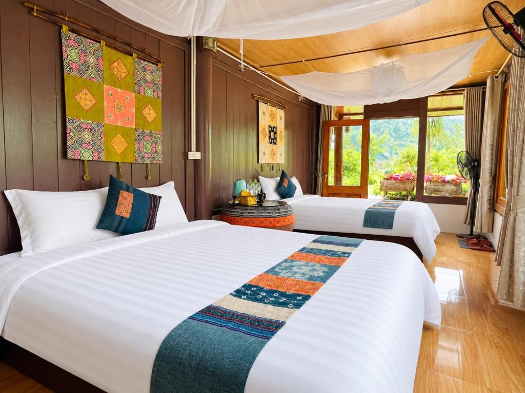 A hotel room with two beds, a large window with a view, a bedside table with a lamp, and a decorative quilt.