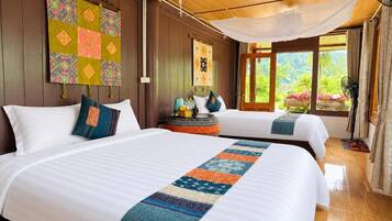 A hotel room with two beds, a large window with a view, a bedside table with a lamp, and a decorative quilt.