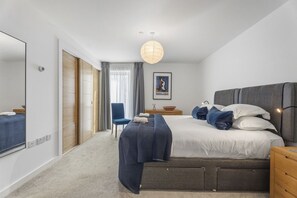 A modern hotel room with a large bed, a bedside table, a chair, a wardrobe, and a large mirror. - The Water of Leith Lookout (Edinburgh)