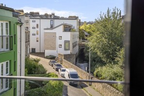 A residential street with a row of parked cars, a white building with a modern design, and a green building on the left. - The Water of Leith Lookout (Edinburgh)