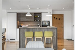 A modern kitchen with a central island, bar stools, and a wooden door. - The Water of Leith Lookout (Edinburgh)