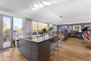 A modern kitchen with a large island, dining area with chairs, a piano, and a view through the glass doors. - The Edinburgh Panorama Penthouse (Edinburgh)
