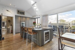 A modern kitchen with a central island, bar stools, and a large window offering a view of the outdoors. - The Edinburgh Panorama Penthouse (Edinburgh)