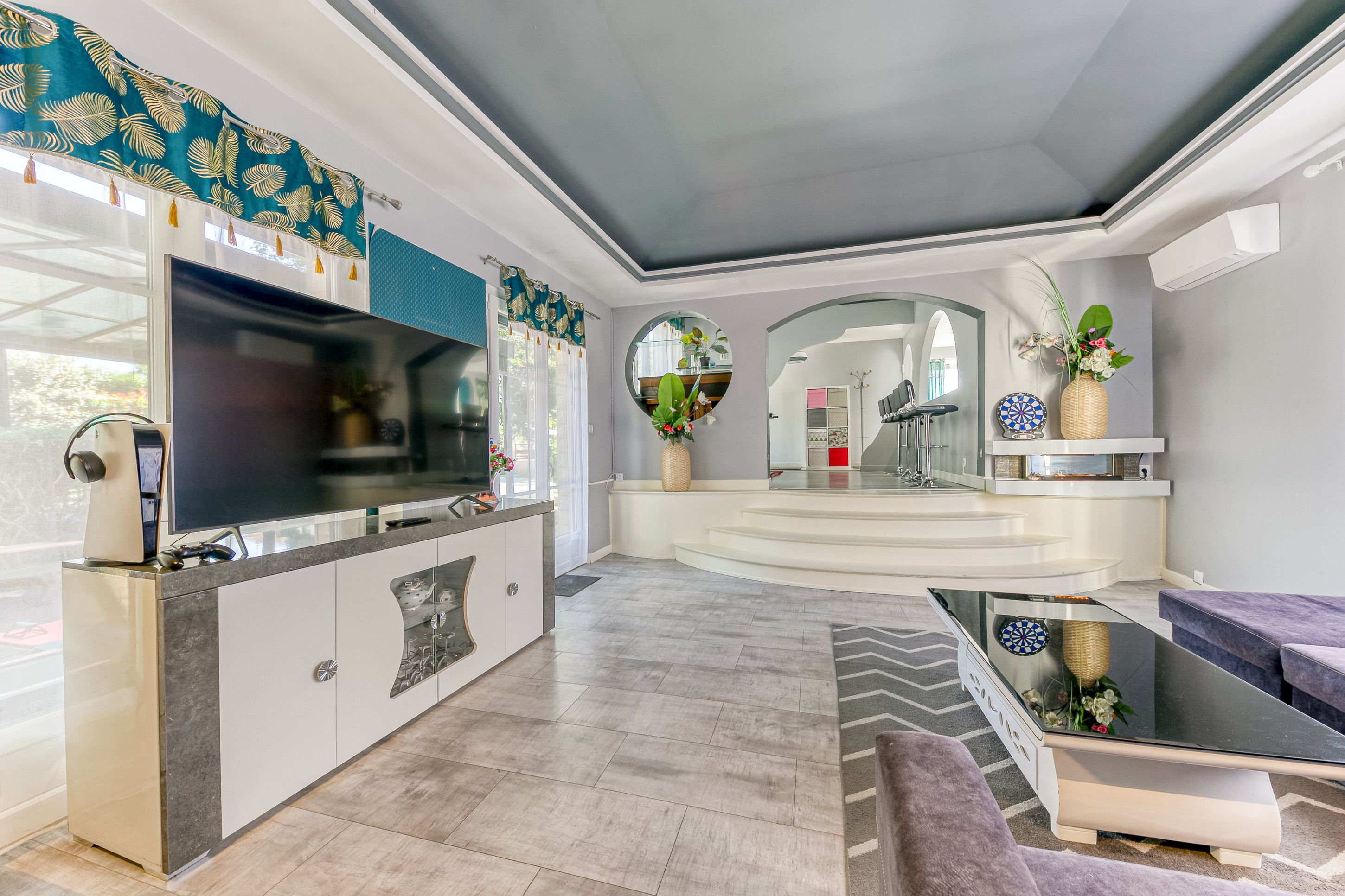 A modern living room with a flat-screen TV, a kitchen area, and a seating area with a sofa and a coffee table.