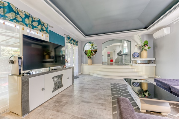 A modern living room with a flat-screen TV, a kitchen area, and a seating area with a sofa and a coffee table.