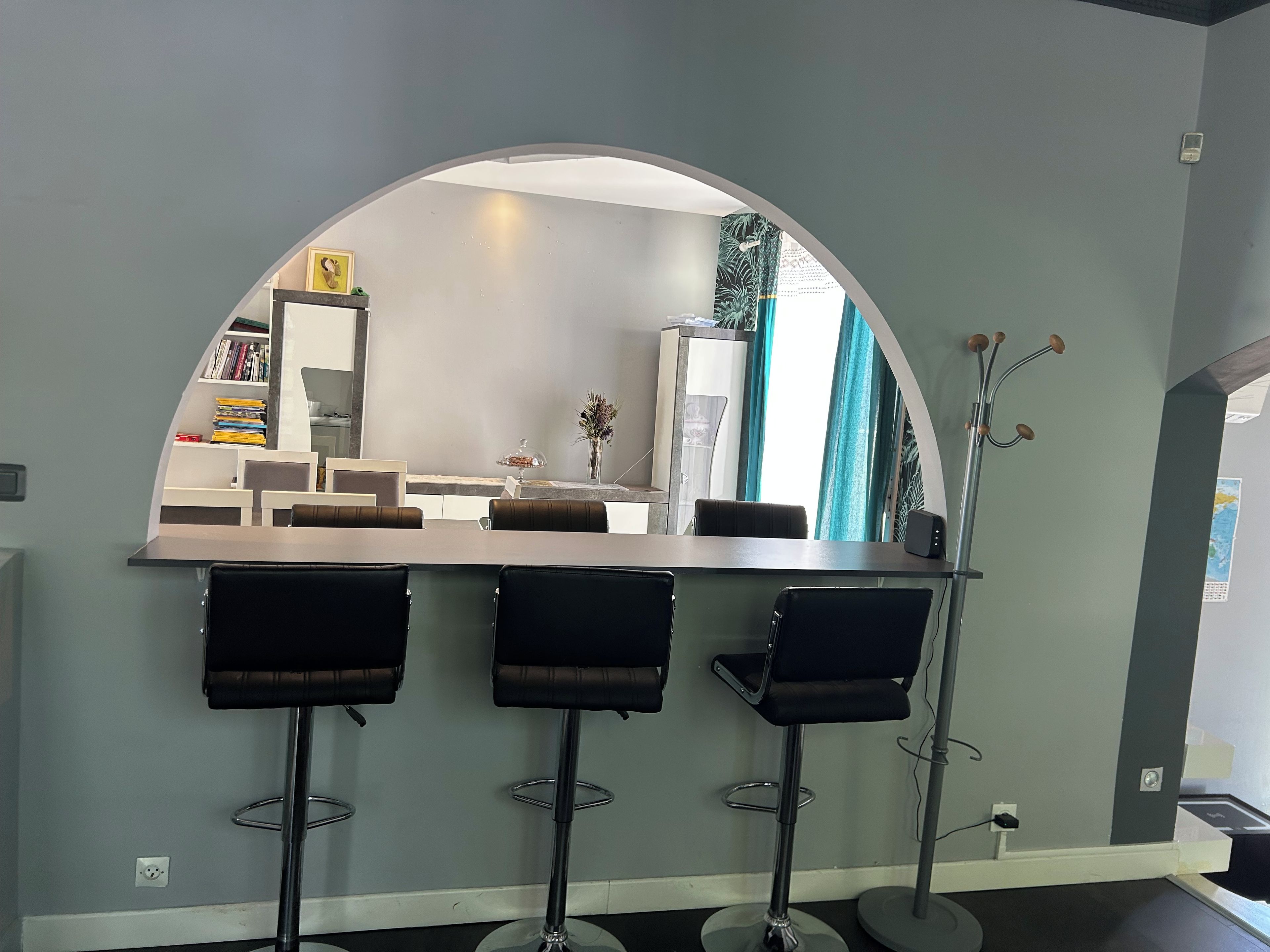 A bar area with a curved mirror, three stools, a small table, and a vase with flowers.