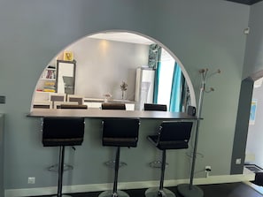 A bar area with a curved mirror, three stools, a small table, and a vase with flowers.