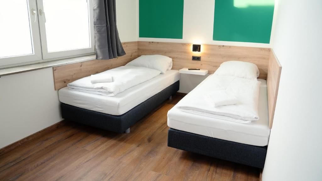 Ein Zimmer mit zwei Betten, einem Nachttisch und einem Fenster mit Vorhängen.