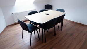 A conference room with a wooden table and black chairs, a white radiator, and a sloped ceiling. - Hive Apartments Lühnde (Algermissen)