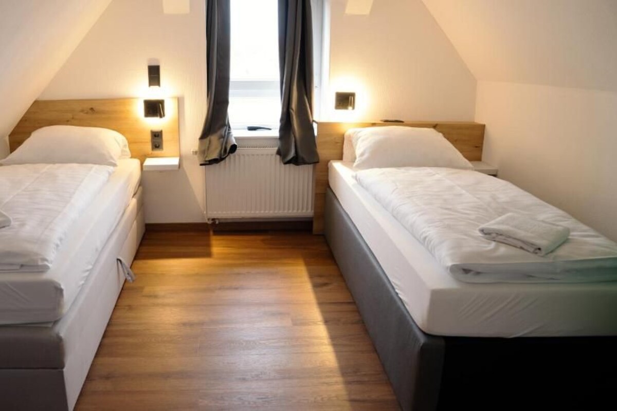 A room with two single beds, wooden flooring, a radiator, and two bedside lamps.