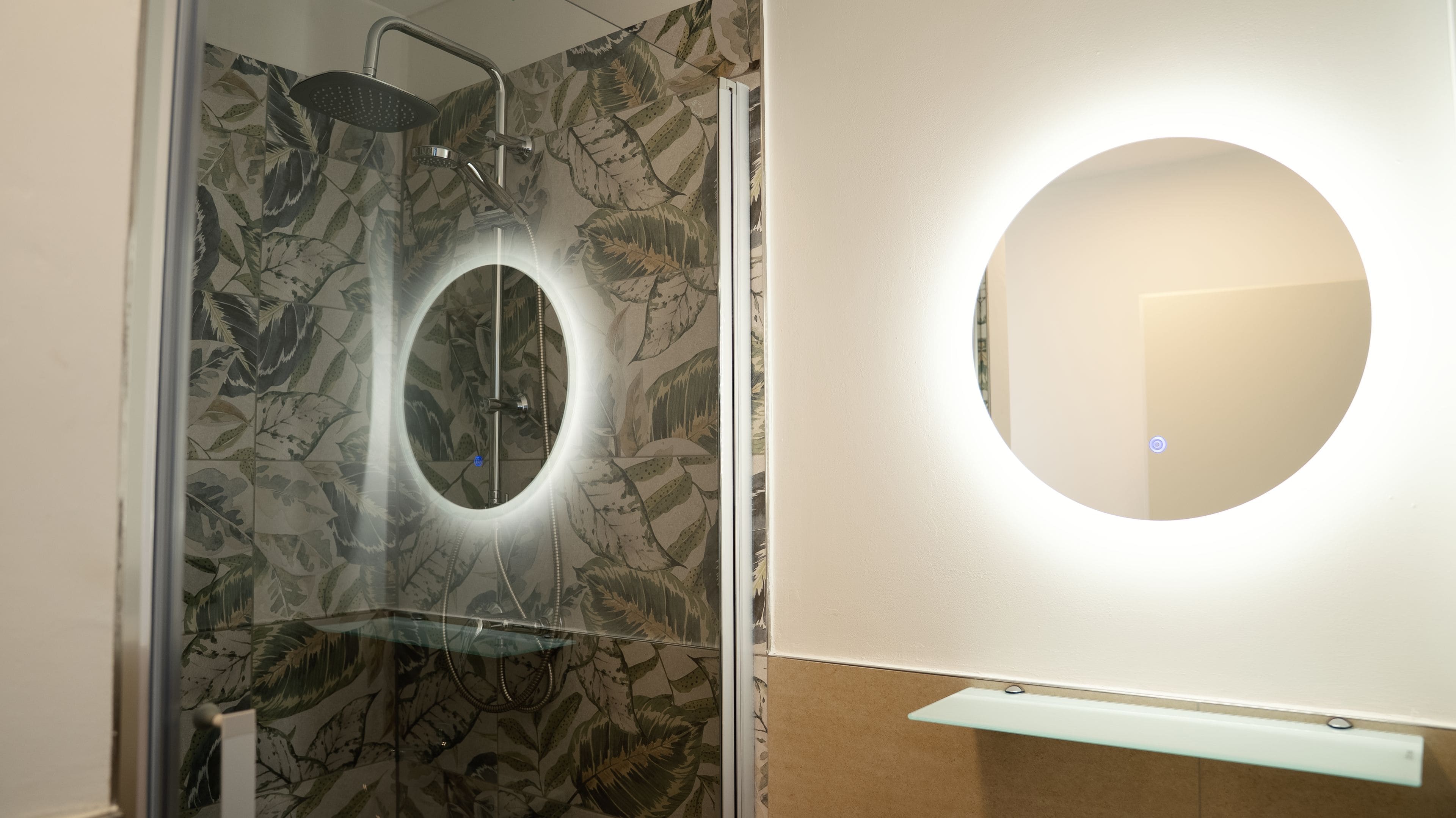 Une salle de bain avec une douche, un miroir rond et un lavabo en verre.