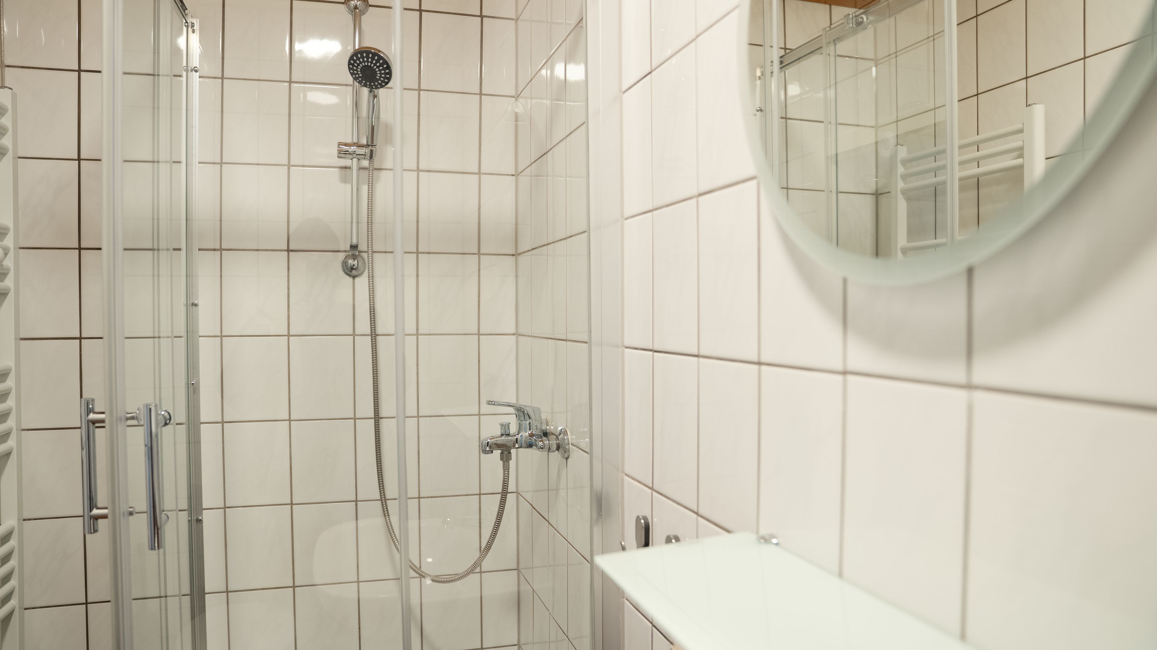 Ein modernes Badezimmer mit einer gläsernen Duschkabine, einer Handbrause und einem wandmontierten Wasserhahn.