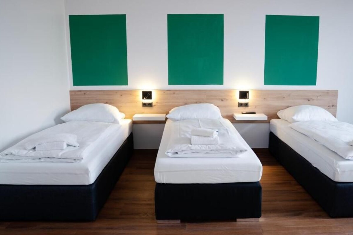 A hotel room with three single beds, each with a wooden headboard, white bedding, and bedside lamps.