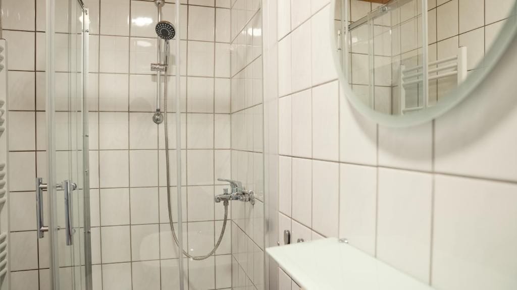 A bathroom with a glass-enclosed shower, a round mirror, and a white sink.