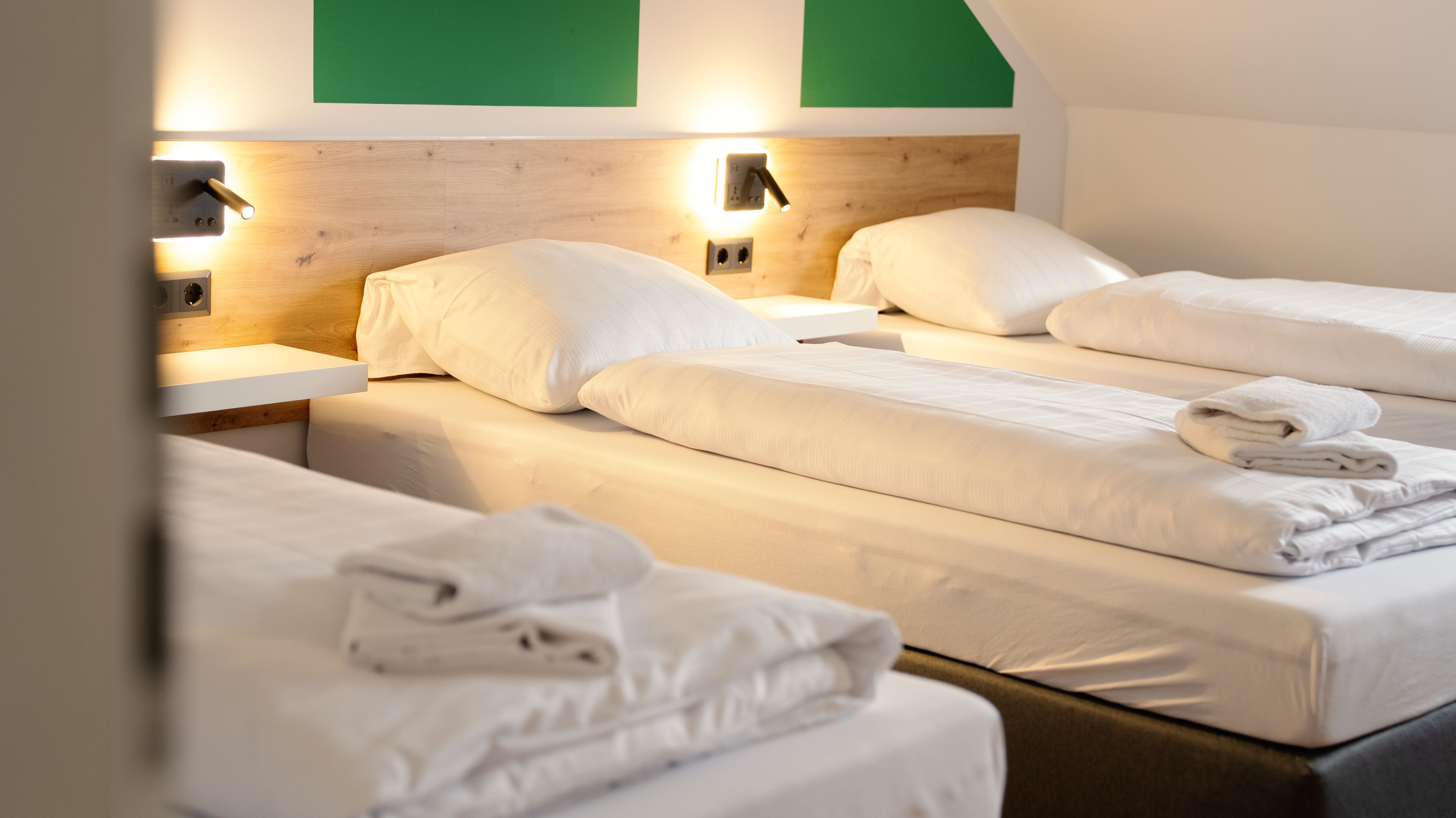 A hotel room with two beds, each with white linens and pillows, a wooden headboard, and wall-mounted reading lights.