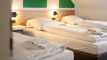 A hotel room with two beds, each with white linens and pillows, a wooden headboard, and wall-mounted reading lights.