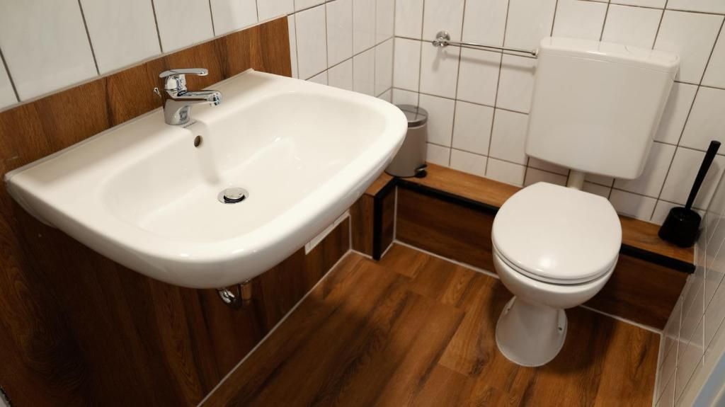 Un baño con lavamanos blanco, inodoro y suelo de madera.