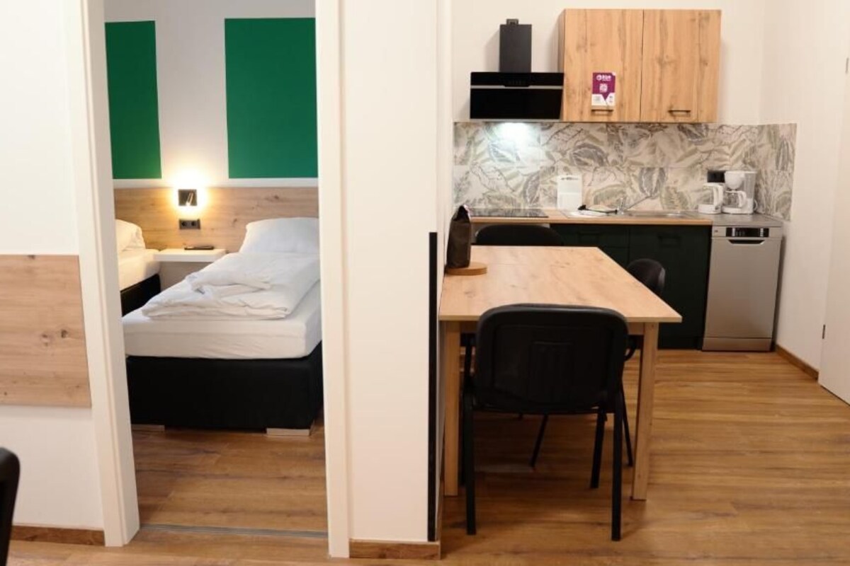 A compact room with a bed, a small dining table, and a kitchenette.