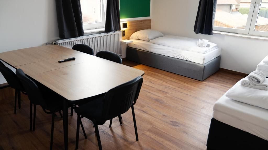 A compact room with a wooden table, two chairs, a bed with a mattress and pillows, and a radiator.