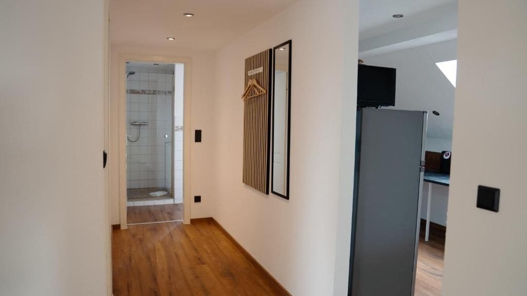 A hallway with a shower, a wooden floor, and a refrigerator.