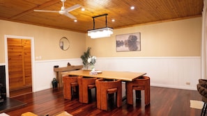 A dining area with a wooden table and chairs, a ceiling fan, a chandelier, and a painting on the wall.