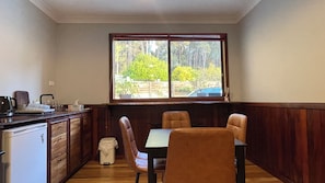 A small kitchen with wooden cabinets, a dining table with chairs, and a window with a view of greenery.