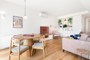 Een moderne woonkamer met een houten eettafel, stoelen, een bank en een televisie.