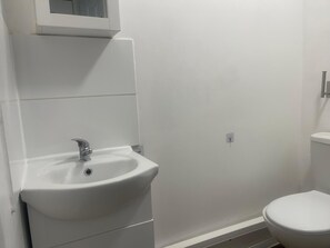 A bathroom with a white sink, a toilet, and a wall-mounted mirror. -  A Studio apartment with a fully equipped kitchenette and Bathroom (Mitcham)