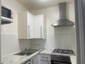 A kitchen with white cabinets, a stainless steel range hood, a microwave, and a gas stove. -  A Studio apartment with a fully equipped kitchenette and Bathroom (Mitcham)