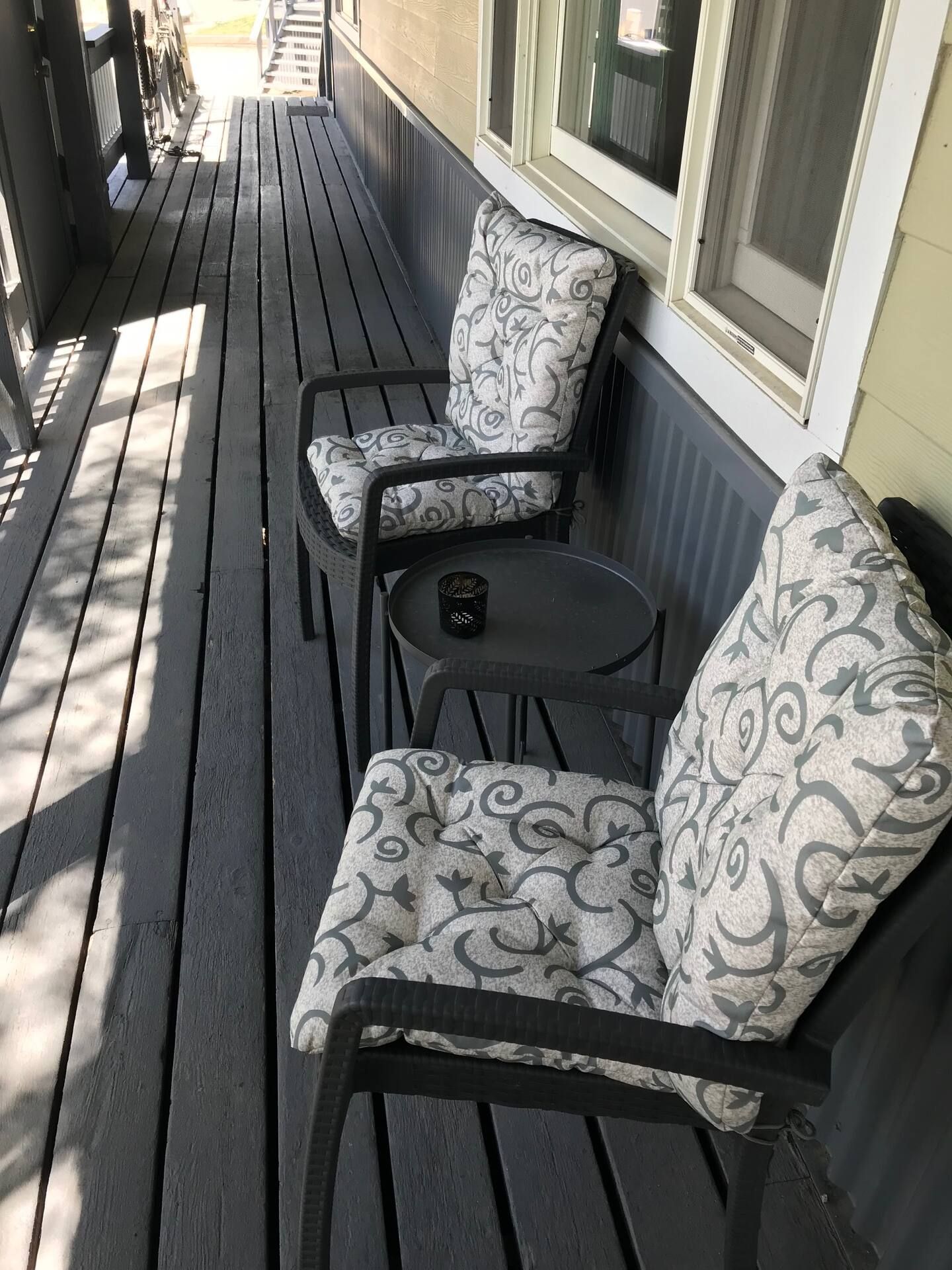A wooden deck with two chairs and a small table, featuring a patterned cushion.