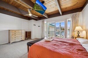 Un dormitorio con cama, cómoda, escritorio y vista a un lago desde un balcón.