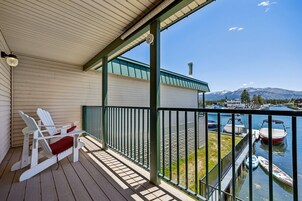 Un balcón con sillas Adirondack, vista de un puerto deportivo con barcos y una montaña al fondo.