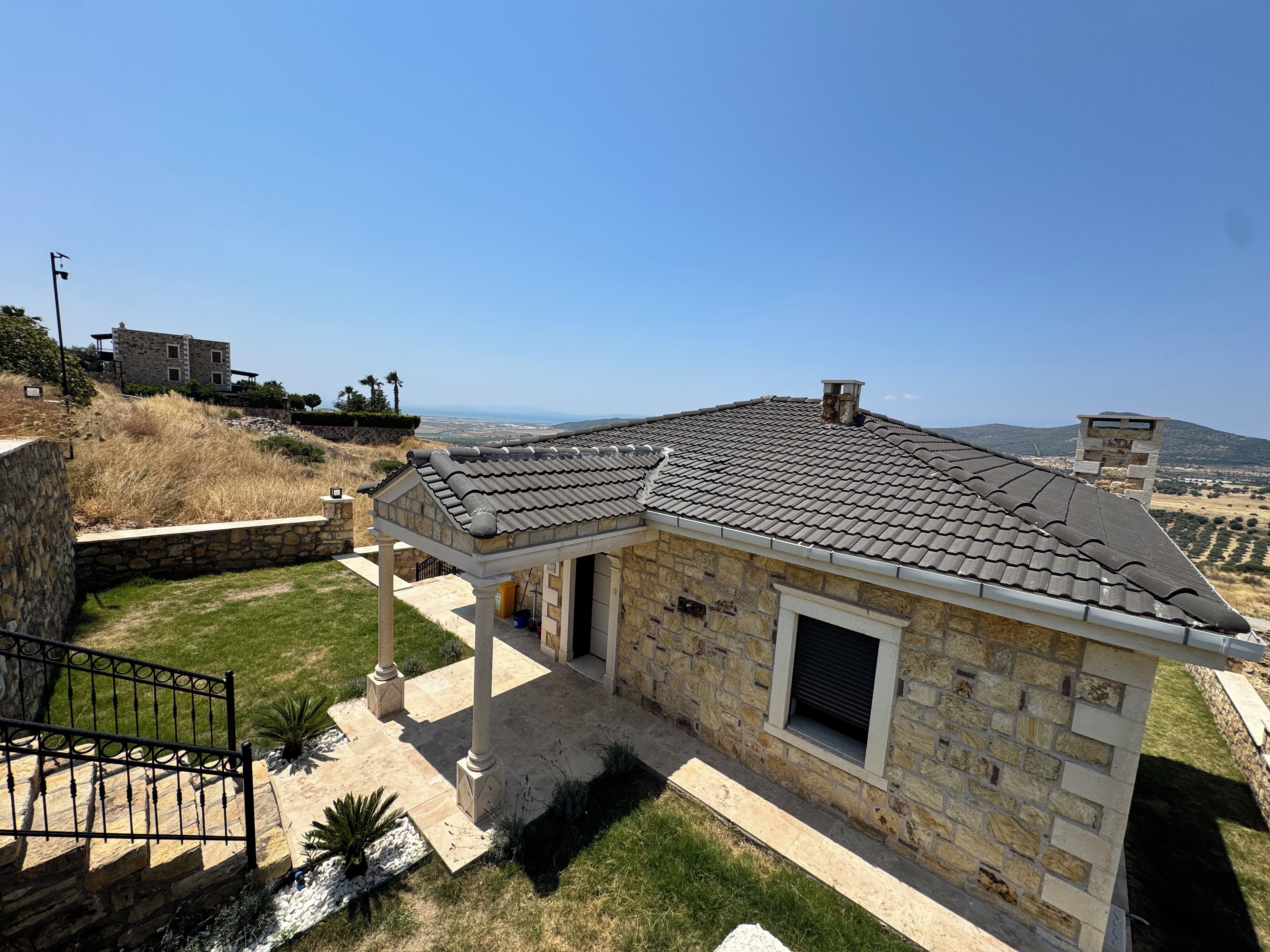 A stone house with a tiled roof, a covered patio, and a view of the countryside.