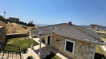 A stone house with a tiled roof, a covered patio, and a view of the countryside.