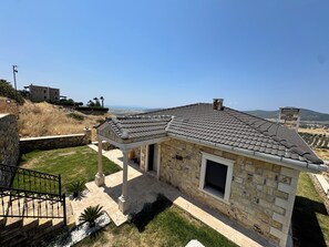 A stone house with a tiled roof, a covered patio, and a view of the countryside.