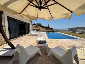 A poolside area with lounge chairs, an umbrella, and a view of the sea. - Foça Taş Villa (foça)
